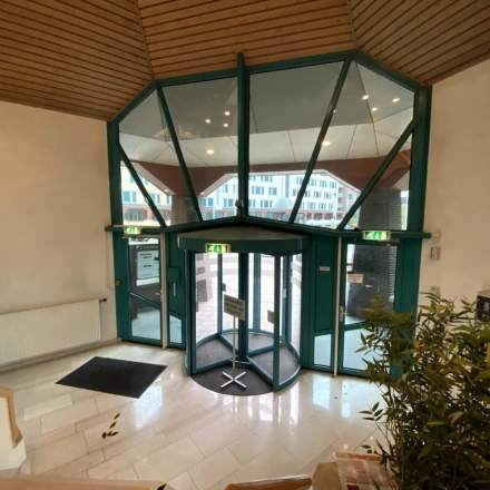 Ingang van een modern kantoorpand aan Loire 104 - 206, Voorburg met glazen draaideur en houten plafond. Ideaal voor wie een kantoorruimte wil huren. Buiten zijn meerdere kantoorgebouwen zichtbaar.