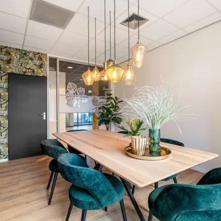 Kantoorruimte huren aan Agro Business Park 22, Wageningen. Gezellige vergaderruimte met houten tafel, stijlvolle stoelen, en opvallende wanddecoratie. Hanglampen creëren een warme sfeer.