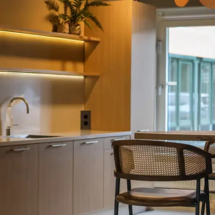 Moderne pantry in een kantoorpand op Vijzelmolenlaan 9, Woerden, met houten keukenkastjes, planten en een stijlvolle hoge stoel aan een bar.