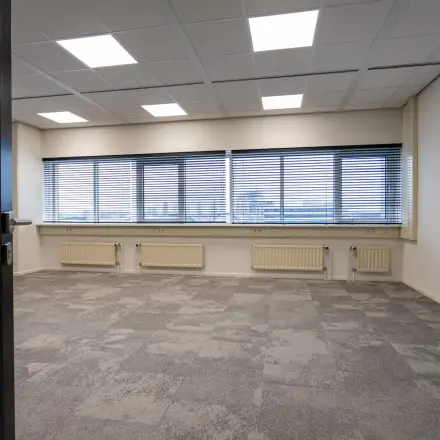 Kantoorruimte te huur in het kantoorpand op Boerhaavelaan 40, Zoetermeer. De ruimte heeft grote ramen met jaloezieën en grijze vloerbedekking.
