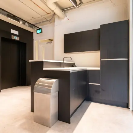 Moderne pantry in kantoorpand aan de Boerhaavelaan 40, Zoetermeer, geschikt voor kantoorruimte huren. Strakke, donkere kasten met een gootsteen en subtiele verlichting. Perfect voor dagelijks gebruik door kantoorpersoneel.