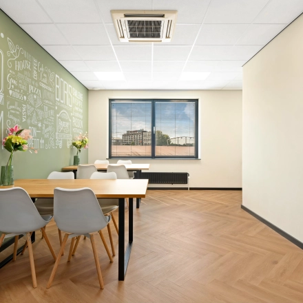 Moderne kantoorpand ingericht als ontmoetingsruimte met houten vloer, groene wanddecoratie en tafel met stoelen. Voor een flexibele kantoorruimte huren in Zwijndrecht, Stationsplein 4.