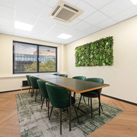 Een lichte vergaderruimte in een kantoorpand op Stationsplein 4, Zwijndrecht, met groene stoelen en een natuurlijke wanddecoratie. Ideale kantoorruimte huren voor professionele bijeenkomsten.