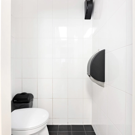 Stijlvolle, wit betegelde toiletruimte met zwarte vloer en moderne voorzieningen in kantoorpand op Stationsplein 4, Zwijndrecht.
