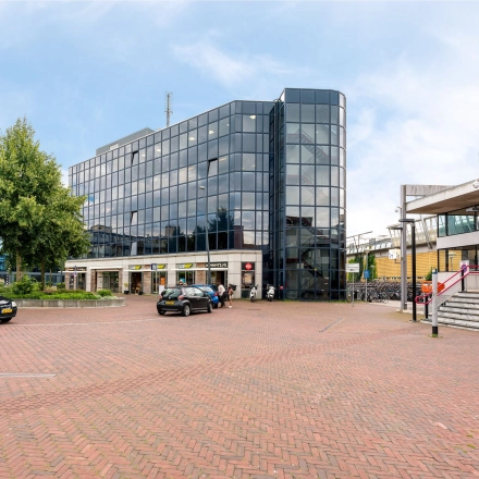 Zakelijk kantoorpand aan het Stationsplein 4 in Zwijndrecht met grote glazen gevel. Het biedt mogelijkheden voor kantoorruimte huren in een moderne omgeving. Buiten zijn geen personen te zien.