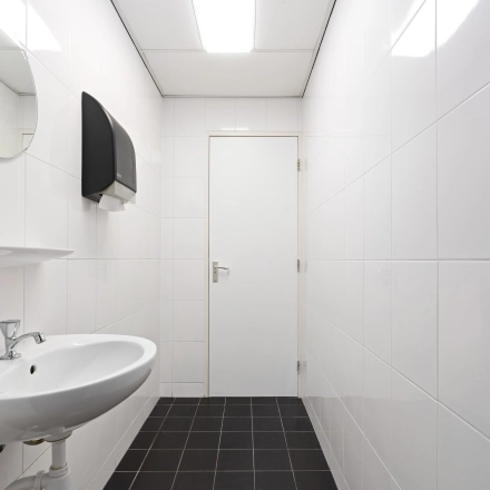 Minimalistische ruimte met witte tegels en wastafel in een kantoorpand aan Stationsplein 4, Zwijndrecht. Ideaal voor bedrijven die kantoorruimte willen huren zonder poespas.