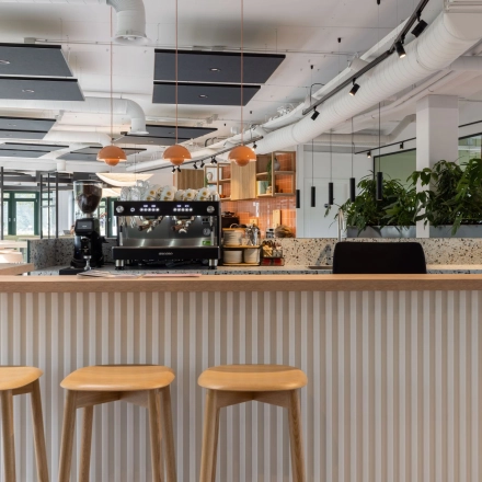 Moderne kantoorruimte huren met open keuken en zitgedeelte op de Hanzelaan 351-361, Zwolle. Gezellige sfeer met houten barkrukken en groene planten. Ideaal voor creatieve kantoren.