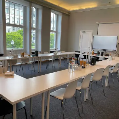 Vergaderruimte te huur op Avenue Palmerston 3, met moderne tafels en stoelen in U-opstelling, ideaal voor meetings in Brussel Europese Wijk. Grote ramen bieden veel natuurlijk licht.
