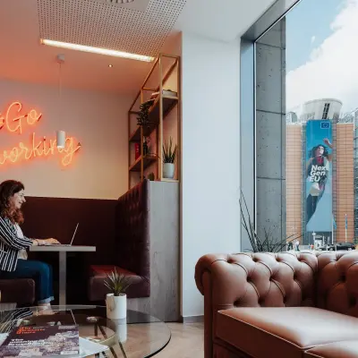 Moderne, gemeubileerde kantoor te huur op het Robert Schumanplein 2-4, Brussel Europese Wijk, met uitzicht op de straat en een persoon die aan een laptop werkt in een gezellige werkruimte.