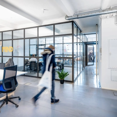 Modernes Büro in Berlin Kreuzberg mit offenen Arbeitsbereichen, Schreibtischen und Glaswänden. Personen arbeiten oder bewegen sich durch den Raum.