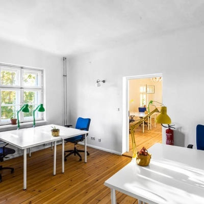 Helles Büro im Berlin Lichtenberg mit großen Fenstern und drei weißen Tischen, ideal zum Büro mieten. Moderne Bürostühle und dezente Dekorationen runden die Einrichtung ab.