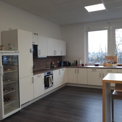 Helle Büroküche zur Miete in München Pasing mit Kühlschrank, Ofen und zwei Barhockern; ideal für Meetings oder Pausen.