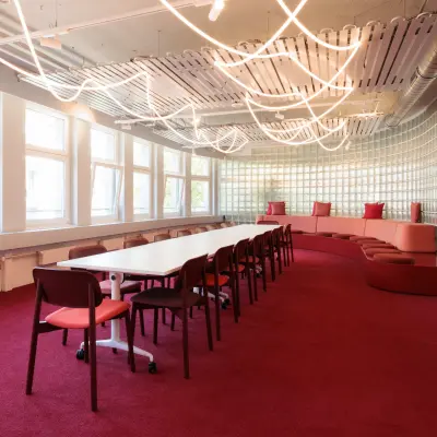 Modernes Büro zur Miete in der Uraniastrasse 31, Zürich City, mit stilvollem Tisch, roten Stühlen und geschwungener Sitzbank auf rotem Teppich.