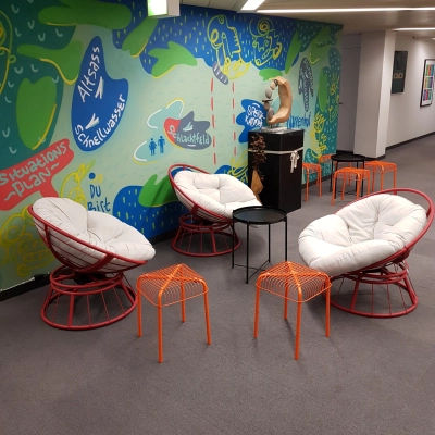 Bunter Loungebereich im Büro am Mythenquai 26, Zürich Enge, mit modernen Sesseln und Hockern vor einer kunstvoll bemalten Wand. Ideal zum Büroraum mieten.