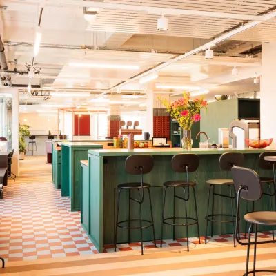 Ein farbenfrohes, modernes Büro mit offenen Arbeitsbereichen und hohen Hockern an einer Theke in Zürich Enge. Perfekt für alle, die Bürofläche mieten möchten.