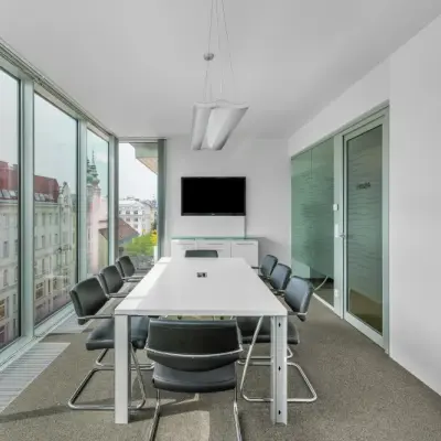 Bright office space rental with large windows offering a city view, located on Mariahilfer Straße 36. The interior is furnished with a conference table and chairs.