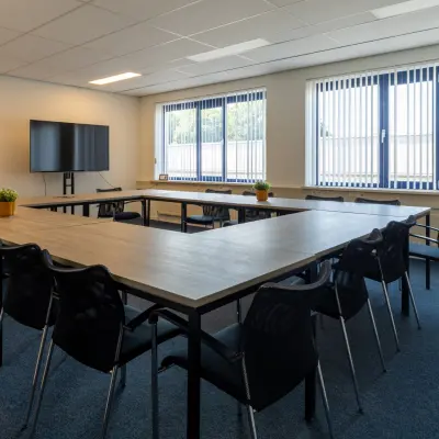 Bright office space for rent in Almelo, featuring a U-shaped conference table with chairs, a flat-screen TV, and large windows providing natural light.