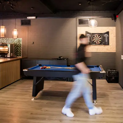 Modern office lounge area with a pool table and a person walking by, featuring stylish lighting and a small kitchen setup in Almere Stad office space rental.