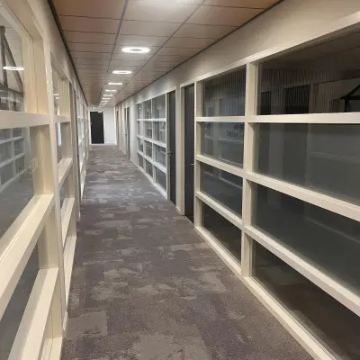 Long hallway with carpeted floor and glass partition walls in an office space for rent at Leidse Schouw 2, Alphen aan den Rijn.