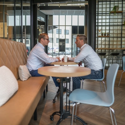 Two people having a business discussion in a stylish furnished office to rent at Maanlander 47, Amersfoort Calveen, featuring modern decor ideal for office space rental.