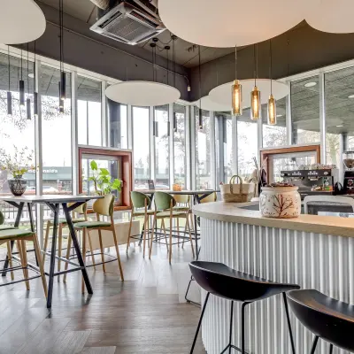 Modern cafe-style furnished workspace at Maanlander 47, Amersfoort Calveen, available for office space rental. Features high tables, chairs, and large windows offering natural light.