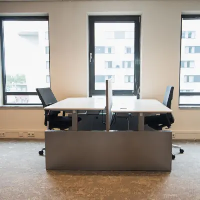 Interior view of a modern office space rental at Ruimtevaart 24, Amersfoort Calveen, featuring two desks and chairs positioned by large windows.