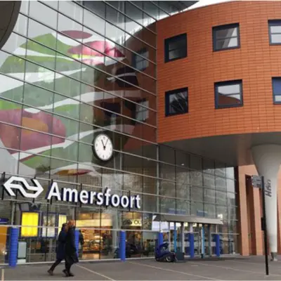 Exterior view of Amersfoort Centraal Station with modern design elements and people walking by.
