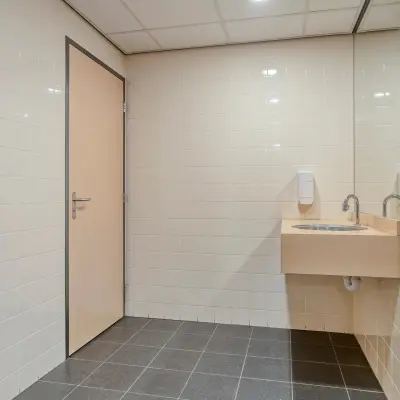 Office restroom with tiled walls, a wooden door, and a sink located at Asch van Wijckstraat 2-4 in Amersfoort Centrum, suitable for office space rental.