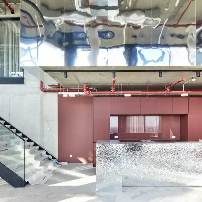 Modern reception area with reflective metallic desk, red accent wall, and industrial elements at H.J.E. Wenckebachweg 230-258, Amsterdam Amstel Business Park, ideal for office space rental.