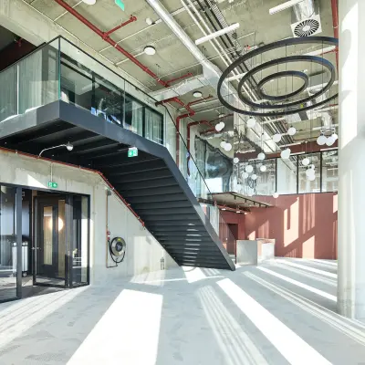 Modern office space with high ceilings and industrial design in Amsterdam Amstel Business Park, featuring large windows and a striking staircase, ideal for office space rental.