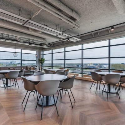 Bright and spacious furnished office interior with round tables and chairs, offering a view over Amsterdam Amstel Business Park, ideal for office space rental.