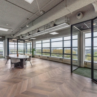 Spacious office to rent at Amsterdam Amstel Business Park, featuring large windows with city views, a round meeting table, and modern furnishings.