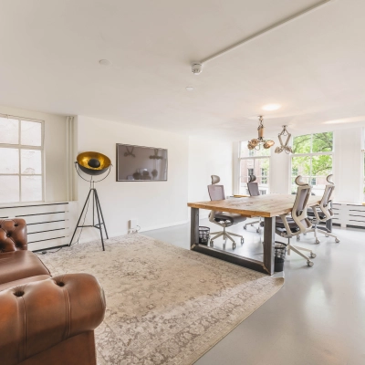 Bright office space for rent at Herengracht 221, Amsterdam Canal Belt, with modern furnishings, including a large wooden table and chairs, facing large windows.