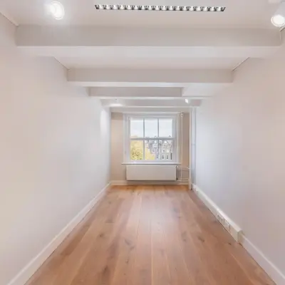 Unfurnished office space available for rent at Herengracht 582-584, Amsterdam Canal Belt, featuring wooden floors and large window with canal views.