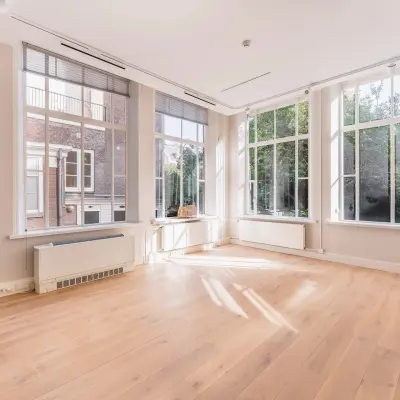 Bright, unfurnished office space available for rent at Herengracht 582-584 in Amsterdam Canal Belt, featuring large windows with garden views and wooden flooring.