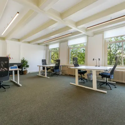 Bright office space with modern desks and chairs, large windows overlooking trees in the Amsterdam Canal Belt.