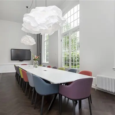 Bright, modern office space rental in Amsterdam Canal Belt, featuring a long table with colorful chairs under unique pendant lights, perfect for meetings.