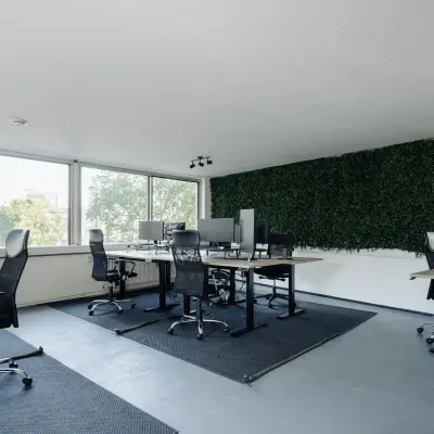 Office space for rent in Amsterdam Canal Belt with modern desks and chairs, large windows providing natural light, and a green wall accent. Located at Weesperstraat 394-396.