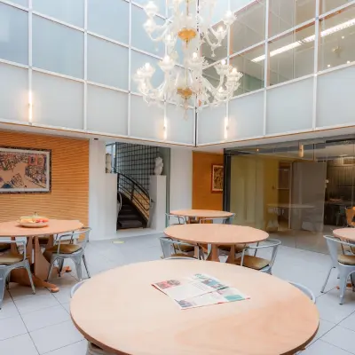 Spacious furnished office space for rent at Kerkstraat 204, Amsterdam Center, featuring round tables and a chandelier, ideal for collaborative work.