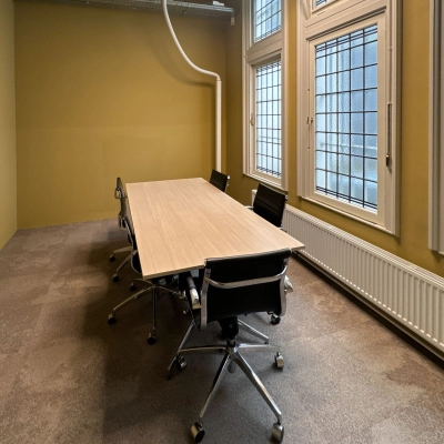 Furnished office space with a long wooden table and six chairs by large windows, available for rent at Nieuwezijds Voorburgwal 104-108 in Amsterdam Center.