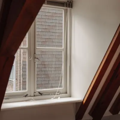 Interior view of office with a slanted ceiling and a window at Prins Hendrikkade 14, Amsterdam Center, ideal for those seeking office space rental with character.