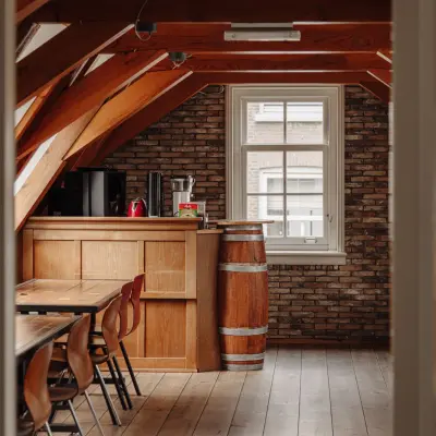 Charming office space rental with wooden beams and brick walls at Prins Hendrikkade 14, Amsterdam Center, featuring a meeting table and kitchenette.