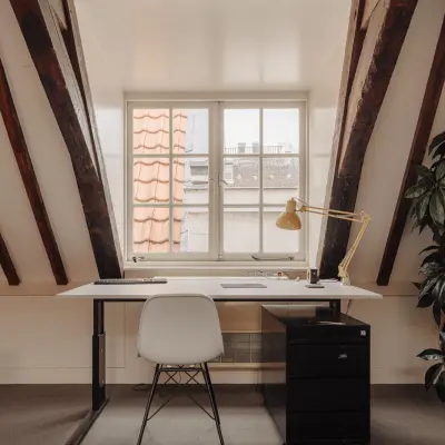 Cozy office space for rent at Prins Hendrikkade 14, Amsterdam Center, featuring a single desk with a lamp and drawers under rustic wooden beams.