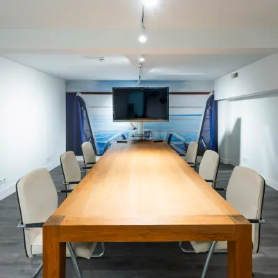 Interior view of a furnished office space for rent at Rokin 105, Amsterdam Center, featuring a wooden conference table surrounded by chairs and a wall-mounted screen.
