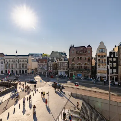 View of Rokin 117, Amsterdam Center, showcasing historic buildings under a bright sun with people walking on the street below.