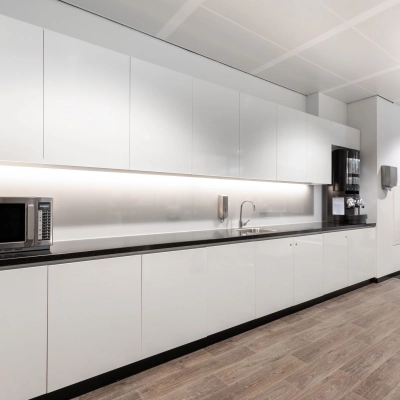Modern office kitchen area at Rokin 92-96, Amsterdam Center, ideal for office space rental, featuring sleek white cabinets, a microwave, and a coffee machine.