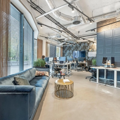 Modern office space at Stadhouderskade 55 in Amsterdam Center with employees working at computers and a seating area with a sofa and table. Ideal for office space rental.