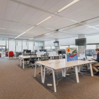 Spacious and well-lit office space rental at Piet Heinkade 95B in Amsterdam East, featuring sleek workstations and modern furnishings. A person is working at a desk by the window.