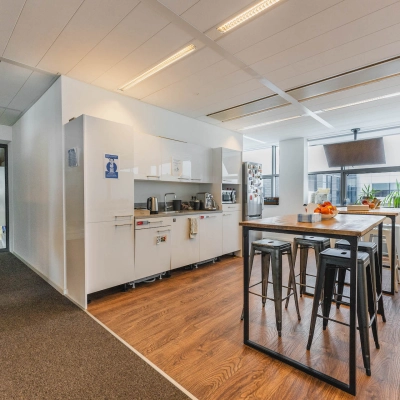 Modern office space in Amsterdam East at Piet Heinkade 95B with sleek wooden floors, a furnished area including a high table and stools, and a kitchenette perfect for office space rental.