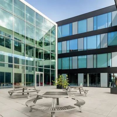 Exterior view of a modern office building at Pedro de Medinalaan 1-9, Amsterdam IJburg, featuring a spacious courtyard with bench seating. Ideal for office space rental.
